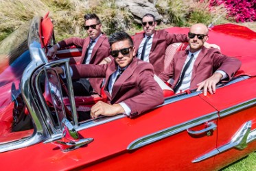 Four members of The Dreamboats sit in a red convertible.