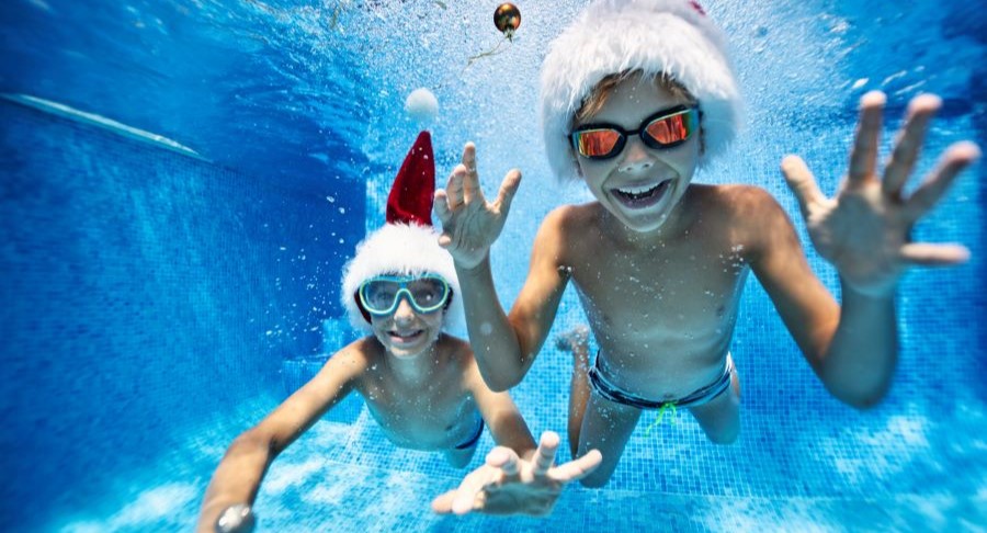 Two children swimming underwater with Santa hats.